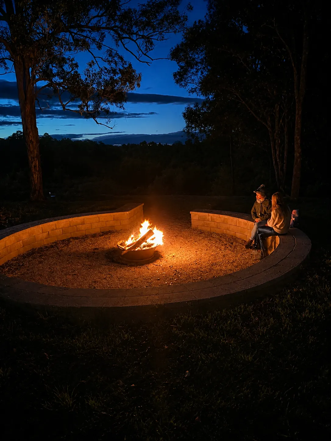 Guests gathered on timber seating around the lit fire pit at dusk at Adeline Estate