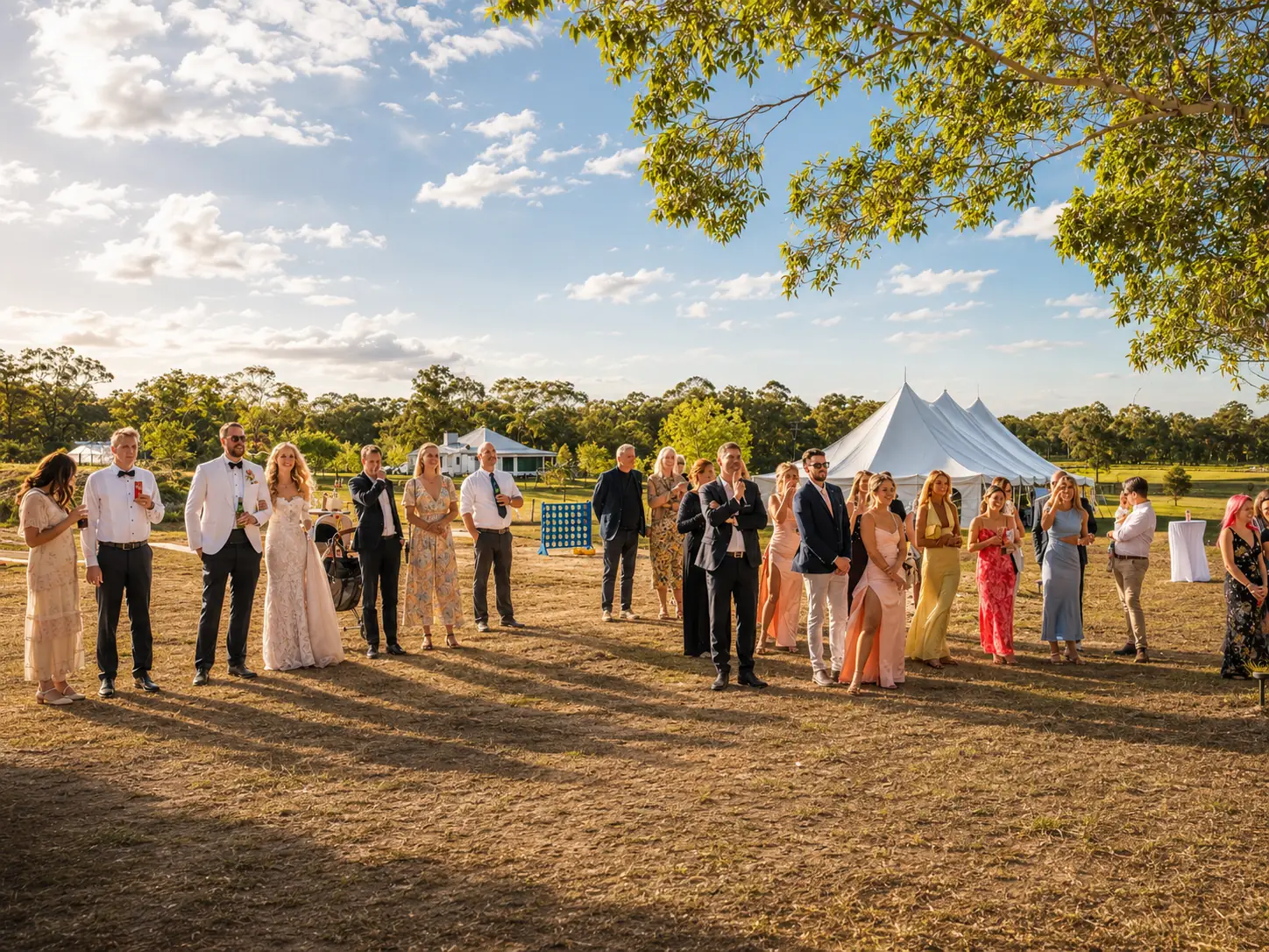 Wedding guests gathered on the lawn with marquee and farmhouse views behind them