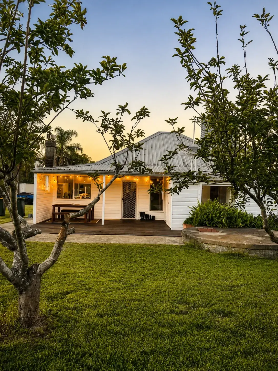 Adeline Estate farmhouse front lawn and orchard at dusk with verandah lights on