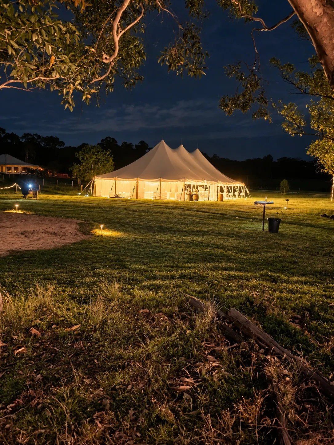Warmly lit white wedding marquee on the lawn beneath a dark evening sky.