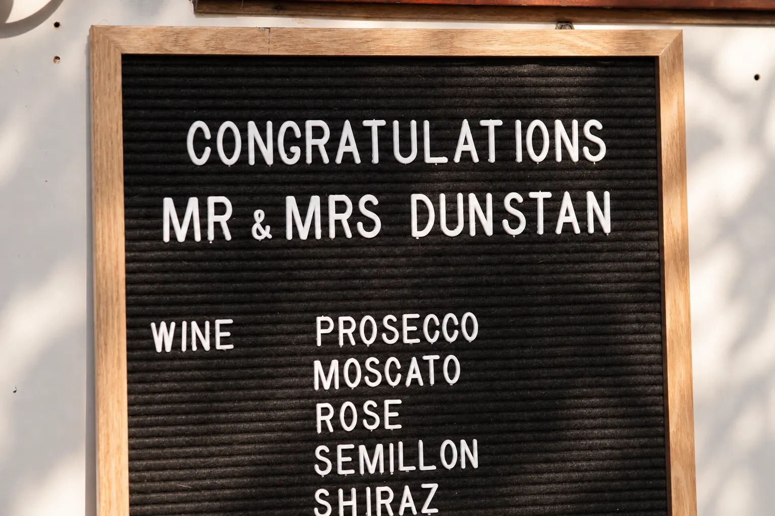 Wood-framed black letterboard displaying wedding congratulations and a selection of wines.