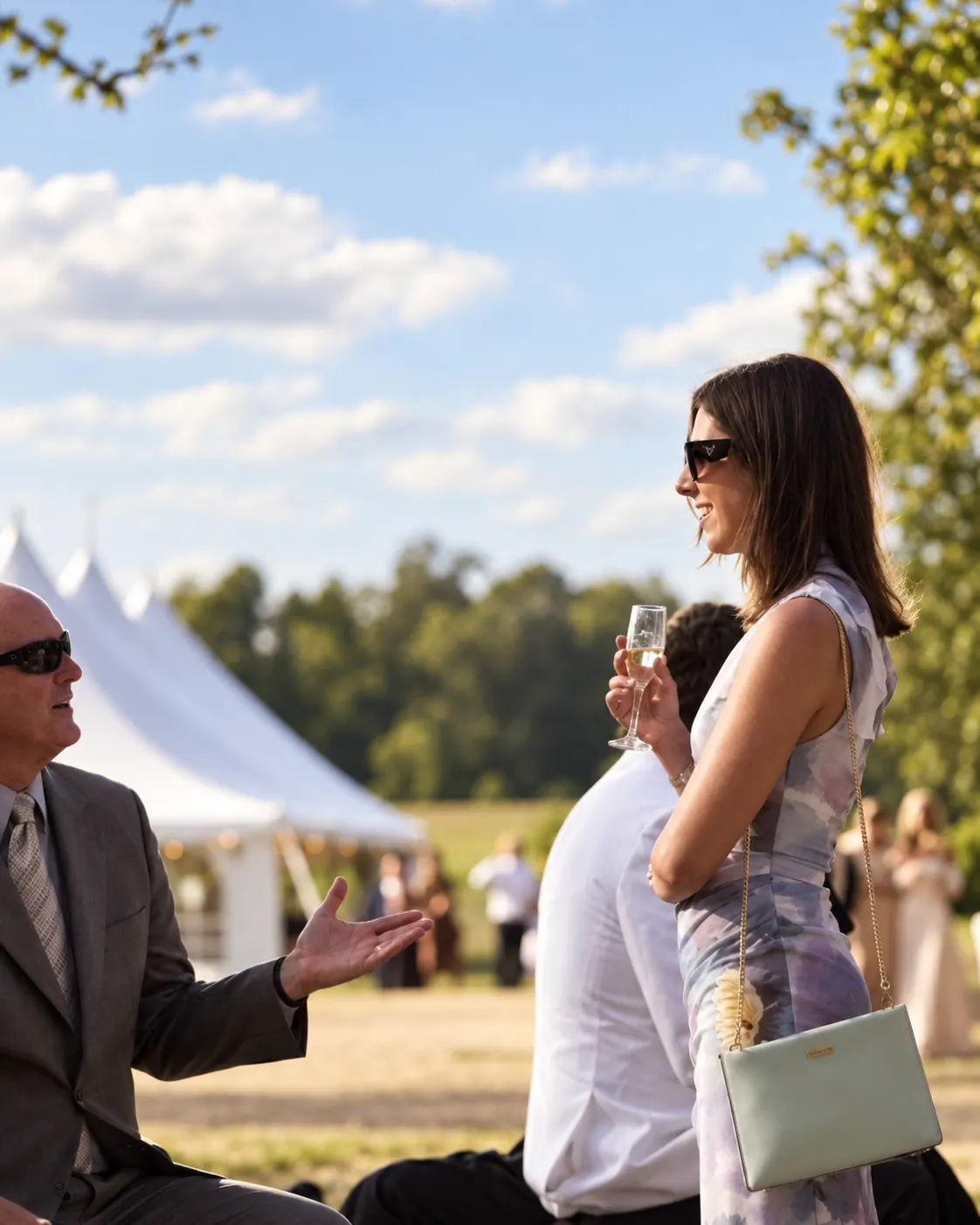 Wedding guests chatting outdoors with a white marquee in the background.