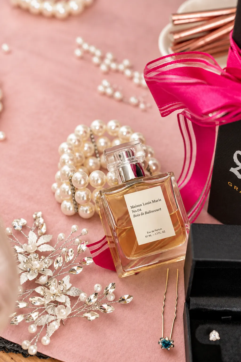 Perfume bottle, pearl jewellery and a decorative bridal hairpiece arranged on pink fabric.